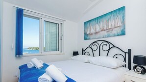 A hotel room with a bed, a window with curtains, a painting of sailboats, and a nightstand with a lamp. - Mljet Gem in Pomena!! (Pomena)