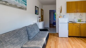 Una sala de estar moderna con un sofá gris, un mueble blanco y una cocina de madera con alacenas y un refrigerador.
