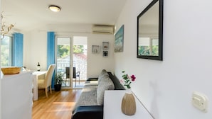 Una sala de estar moderna con un sofá, una mesa de comedor con sillas, una pequeña mesa blanca con un florero y un espejo grande en la pared.