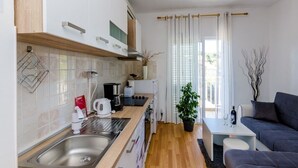 A compact kitchen with a sink, stove, and modern appliances, a dining area with a table and chairs, and a living area with a sofa and a potted plant. - Mljet Pearl in Pomena,National Park Mljet (Mljet)