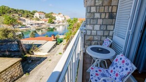 A balcony with a view of a river and buildings, a small table and two chairs, and a stone wall. - Mljet Pearl in Pomena,National Park Mljet (Mljet)