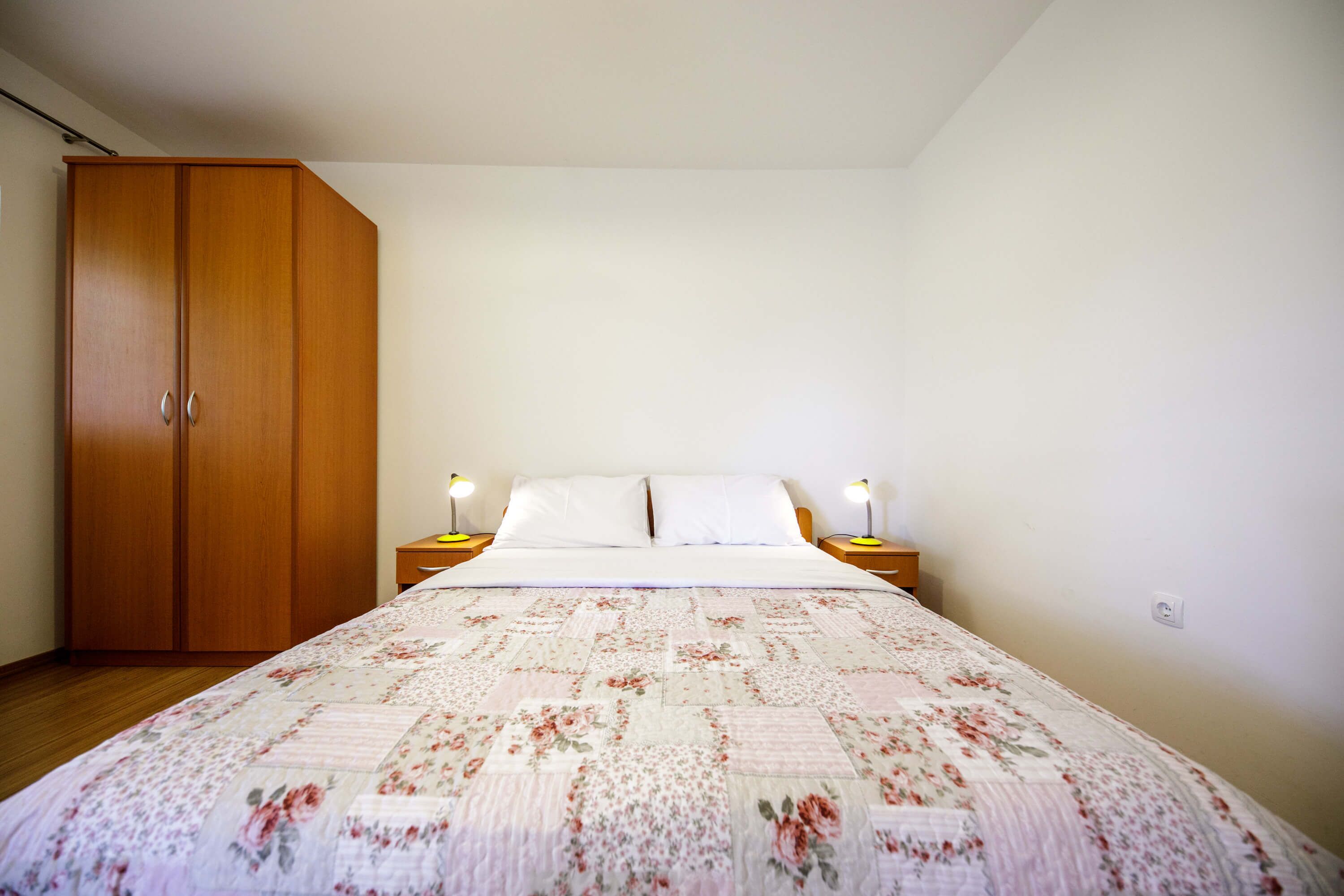 A bedroom with a large bed, a wooden wardrobe, and two bedside tables with lamps.