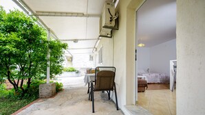 An outdoor patio with a table and chairs, a covered area, and a view into a room with a bed and a nightstand. - Charming studio with garden terrace (Dubrovnik)