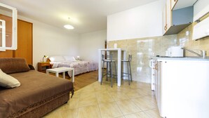 A compact room with a bed, a small table, two chairs, a kitchenette, and a bathroom. - Charming studio with garden terrace (Dubrovnik)