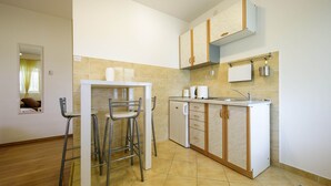 A compact kitchen with a sink, cabinets, and a small refrigerator. There are two metal chairs and a table in the adjacent dining area. - Charming studio with garden terrace (Dubrovnik)