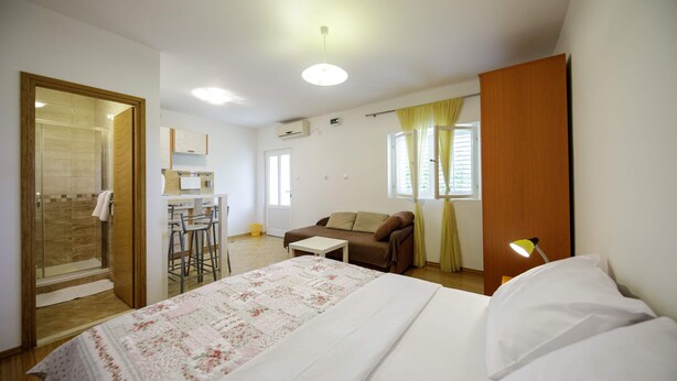 A bedroom with a bed, a bedside table, a lamp, a sofa, a small table, and a shower area. - Charming studio with garden terrace (Dubrovnik)