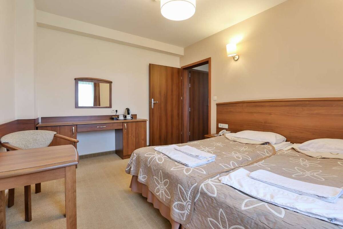 A hotel room with a wooden desk, two beds with floral bedding, a mirror, and a door.