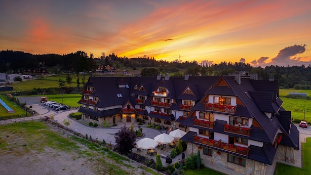 A large, multi-story hotel with a traditional European architectural style, featuring a courtyard with outdoor seating and a parking area. - Pensjonat pod Kotelnica (Bukowina Tatrzanska)