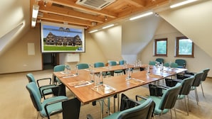 A conference room with a large table, teal chairs, and a projector screen displaying a building image. - Pensjonat pod Kotelnica (Bukowina Tatrzanska)