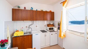 A small kitchen with wooden cabinets, a microwave, a sink, and a window with a view of the sea. - apt Dubrovnik,sea view,near Old tow (Dubrovnik)
