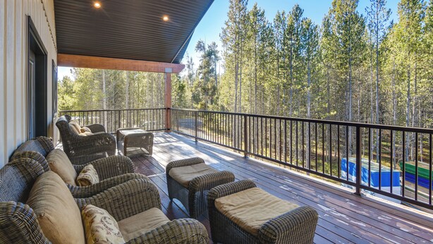 A covered deck with wicker furniture and a view of a forest. - Outdoor Adventure Hub ~ 20 Miles to Yellowstone! (Island Park)