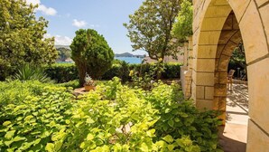 A garden with a stone archway, lush greenery, and a view of the sea. - White Stone Steel - 2 Bedroom Apartment with Terrace and Sea View (Dubrovnik)