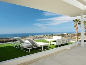 Relax on the ocean-facing terrace with a clear view of the coastline, surrounded by a well-manicured lawn and comfortable lounge seating.