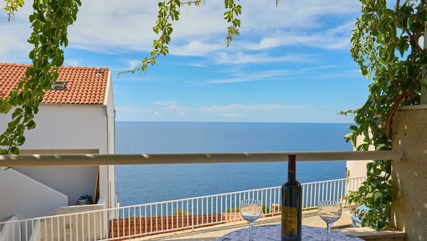 Balcón con mesa, botella de vino y copa, con vistas al mar.