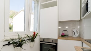Une cuisine moderne avec des meubles blancs, un four encastré, une bouilloire et une fenêtre agrémentée de plantes.