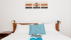 Un lit bien fait, avec une literie blanche et bleue, une paire de serviettes enroulées et une œuvre d’art accrochée au mur au-dessus.