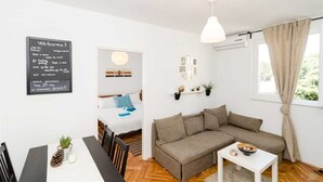 Un salon moderne avec un canapé, une table à manger et des chaises, un luminaire suspendu et une fenêtre avec des rideaux.