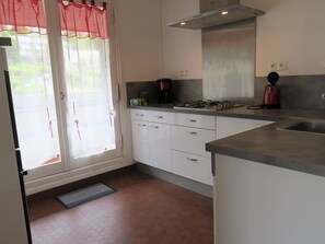 A kitchen with white cabinets, a stainless steel sink, a gas stove, and a red kettle.