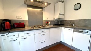 A modern kitchen with white cabinets, a stainless steel range hood, a red kettle, and a dishwasher. - 3* Apartment with terrace and parking, steps from Trestraou Beach in Perros-Guirec (Perros-Guirec)