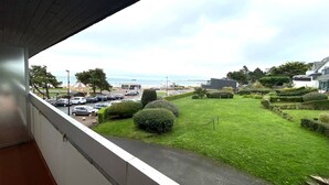 A view from a balcony overlooking a well-maintained lawn, a parking area, and a beach in the distance. - 3* Apartment with terrace and parking, steps from Trestraou Beach in Perros-Guirec (Perros-Guirec)