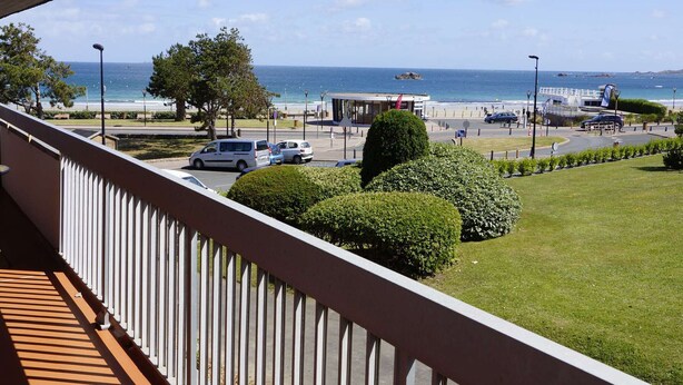 A balcony with a view of the sea, a parking area, and a building with a red flag. - 3* Apartment with terrace and parking, steps from Trestraou Beach in Perros-Guirec (Perros-Guirec)
