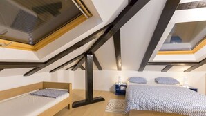 Ein Schlafzimmer mit schrägem Dach, Dachfenstern, einem Bett, Nachttischen und einem kleinen Teppich.