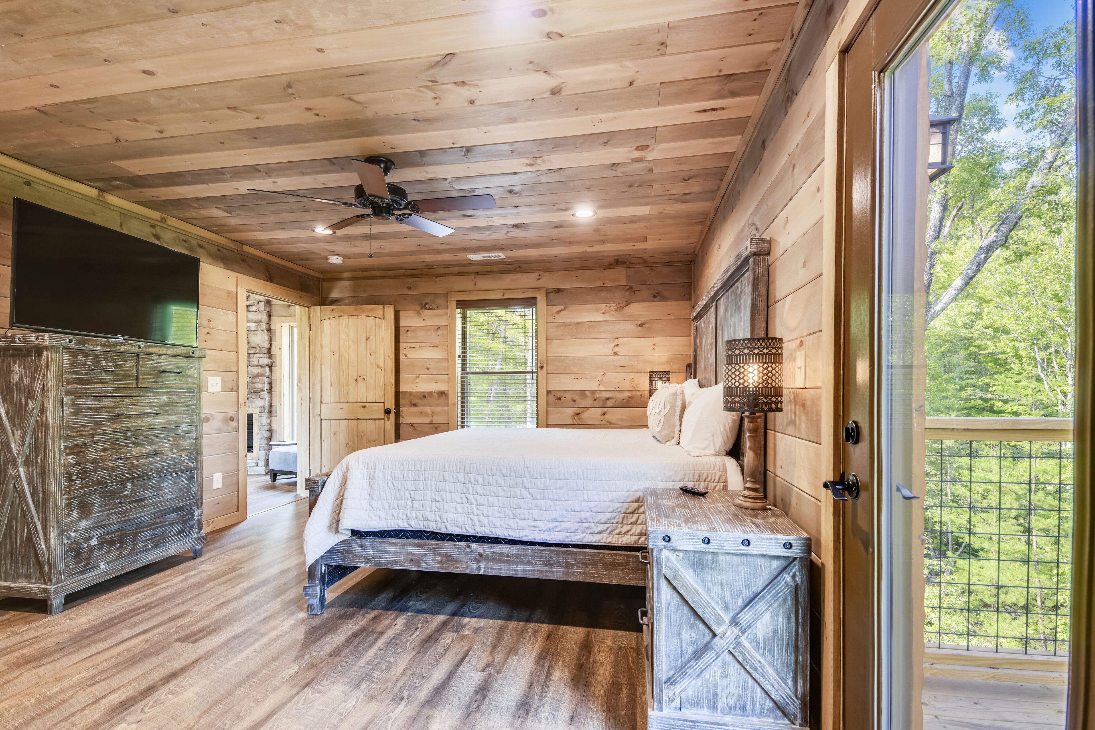 A wooden cabin bedroom with a bed, a dresser, and a large window.