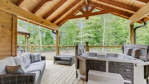 A covered outdoor deck with a hot tub, wicker furniture, and a stone bench.