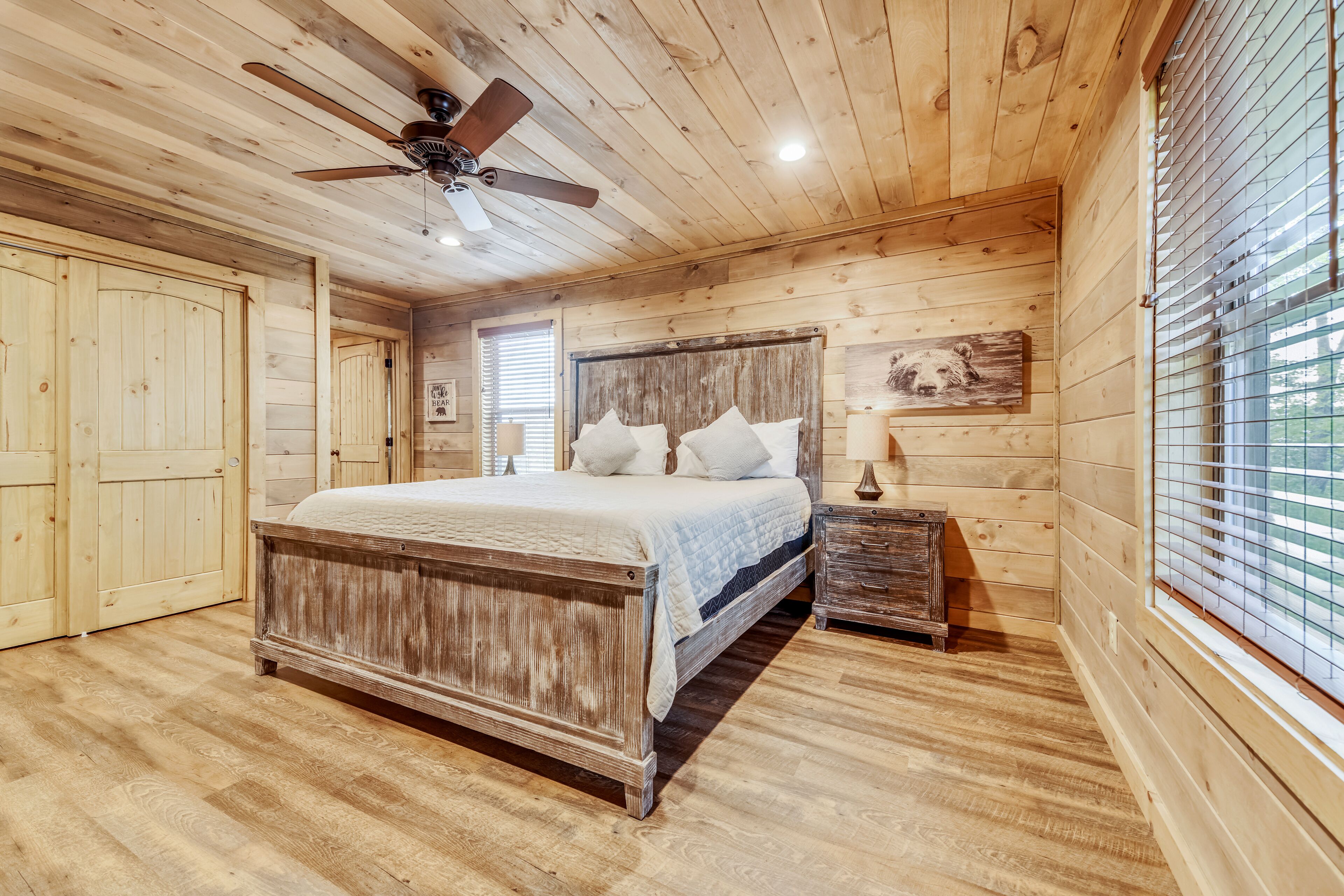 A wooden cabin bedroom with a bed, a ceiling fan, and a window with blinds.
