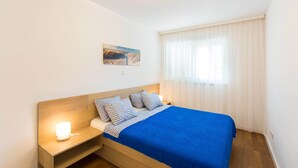 Una camera da letto con un letto, un comodino con una lampada, una finestra con tende leggere e un quadro appeso al muro.
