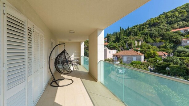 Un balcone con un'amaca, ringhiera in vetro e vista su una collina con edifici.