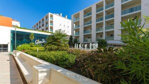 Un hotel moderno con varios pisos, fachada de vidrio y un jardín ajardinado con fuente de agua.