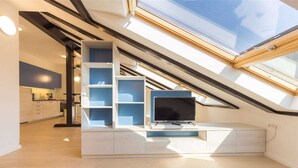 Un loft moderno con tragaluz, estanterías empotradas y un televisor de pantalla plana.