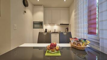 A dining area with a glass table, a bowl of fruit, and a basket of snacks.