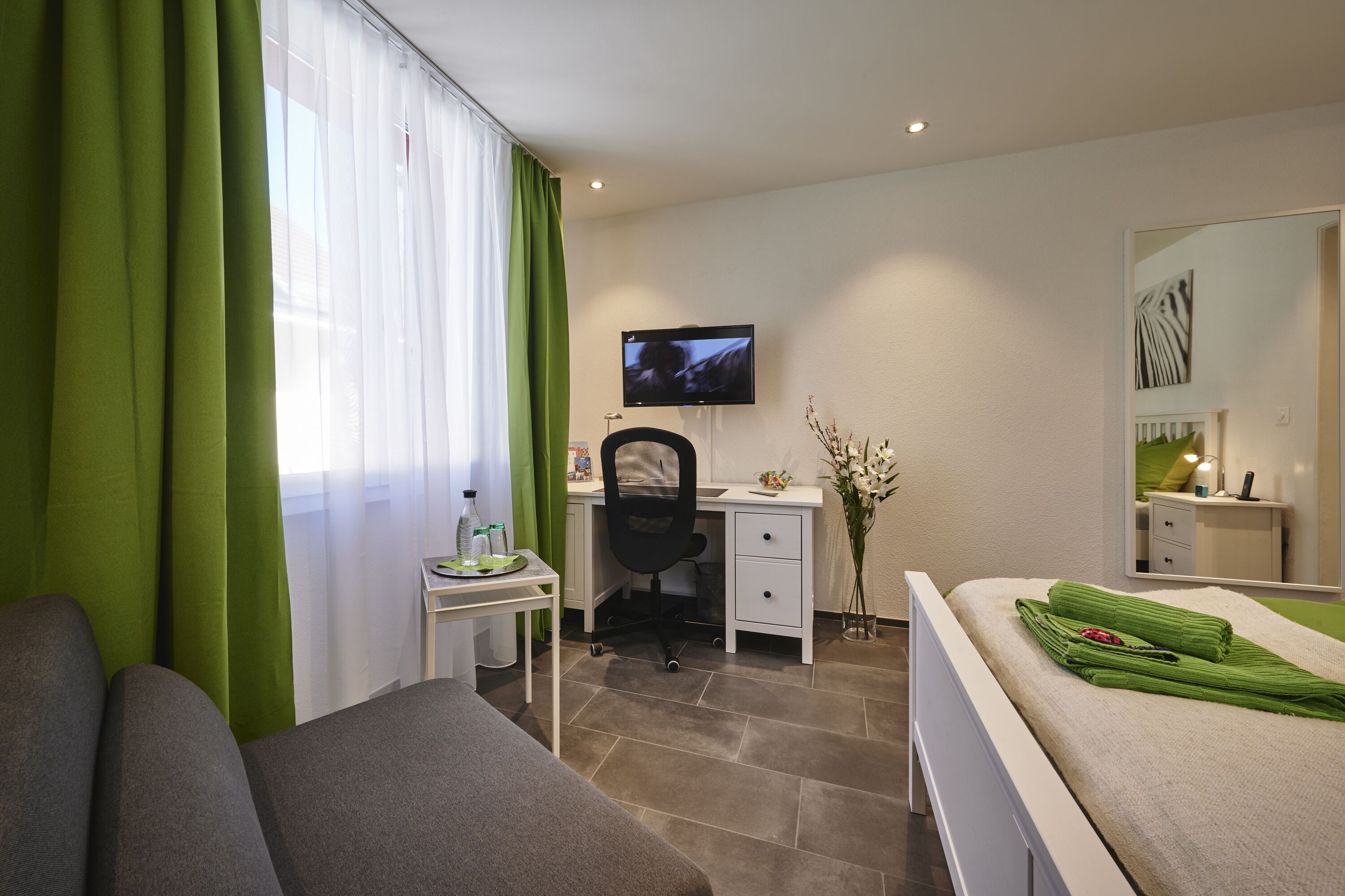 Une chambre d’hôtel équipée d’un lit, d’un bureau, d’une chaise, d’une télévision et d’un miroir.