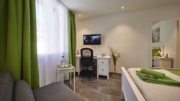 A hotel room with a bed, a desk, a chair, a TV, and a mirror.