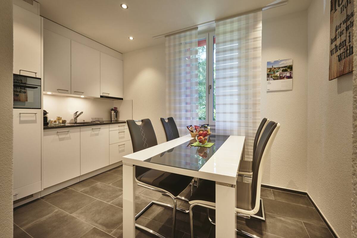 A modern kitchen with white cabinets, a glass-top dining table, and black chairs.
