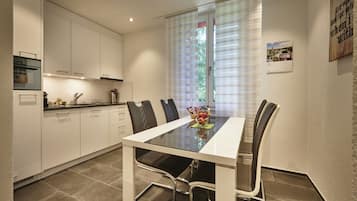 A modern kitchen with white cabinets, a glass-top dining table, and black chairs.