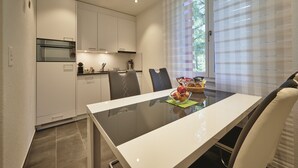 A modern kitchen with white cabinets, a built-in oven, and a dining area with a glass table and chairs.