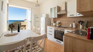 Cocina moderna con vista al mar, que cuenta con muebles blancos, encimera de madera y electrodomésticos básicos.