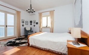 A bedroom with a large bed, a wooden nightstand, a desk, a chair, a cowhide rug, and a balcony view.