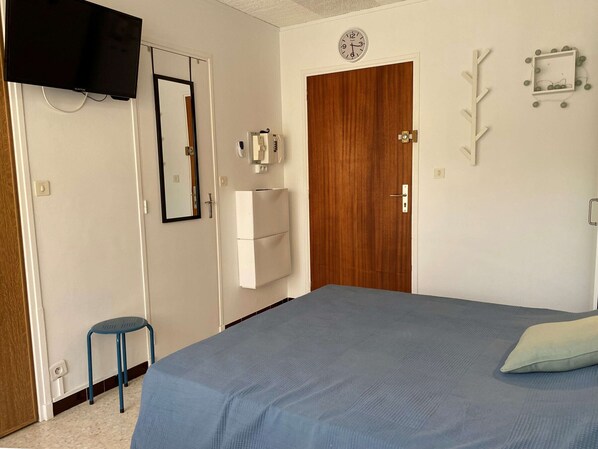 A bedroom with a bed, a mirror, a clock, a wardrobe, and a small stool.