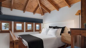 Un dormitorio con techo de madera, una cama con ropa de cama blanca, una mesita de noche y vista al mar a través de las ventanas.