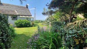 Una casa con un camino de jardín que lleva a la entrada, rodeada de follaje y plantas con flores.
