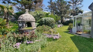 Un jardín con una estructura de piedra, un invernadero de cristal y un césped.