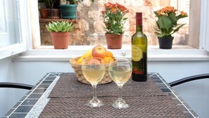 A table with two wine glasses and a bottle of wine, a bowl of fruit, and potted plants on a windowsill. - STUDIO INN - heart of the city! (Dubrovnik)