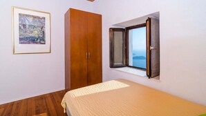 Une chambre à coucher avec un lit, une armoire en bois, un tableau encadré au mur et une fenêtre donnant sur un paysage.