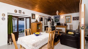 Un salon chaleureux avec un plafond en bois, un coin repas agrémenté d’une nappe en dentelle et un canapé en cuir noir.