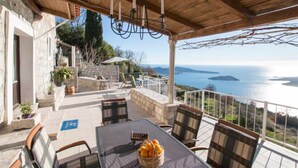 Un espace extérieur abrité, avec une table et des chaises, offrant une vue panoramique sur la mer et les îles.