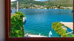Vista a través de una ventana de un lago con un bote amarrado, vegetación y un pueblo lejano.